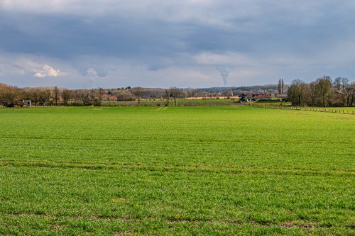 Free Lush green field under a dramatic cloudy sky in a rural landscape, ideal for nature and travel themes. Stock Photo