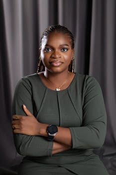 Portrait of a confident African woman in a green dress, seated with arms crossed.