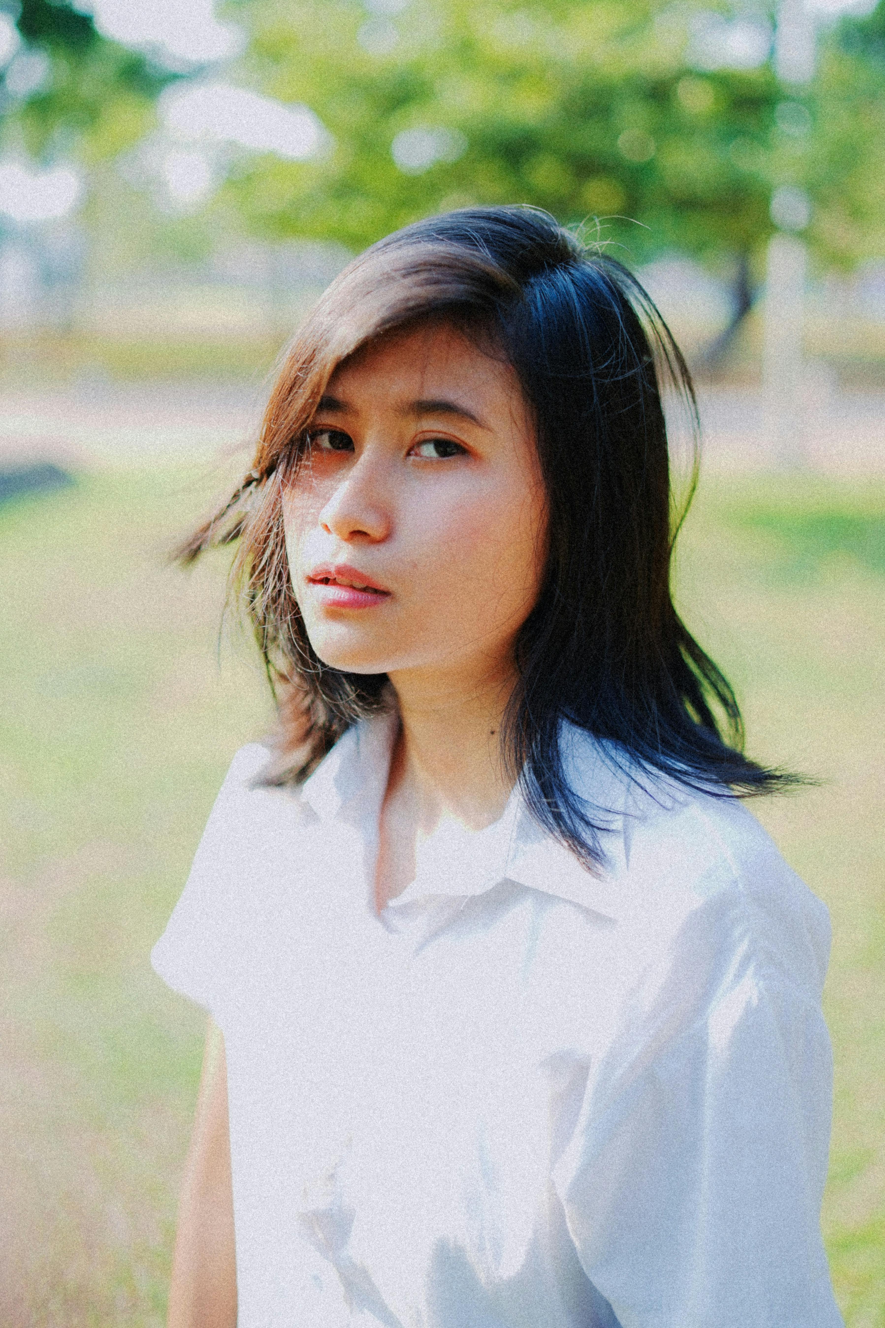 阳光明媚的公园里，一位穿着白衬衫的年轻女子正看着镜头