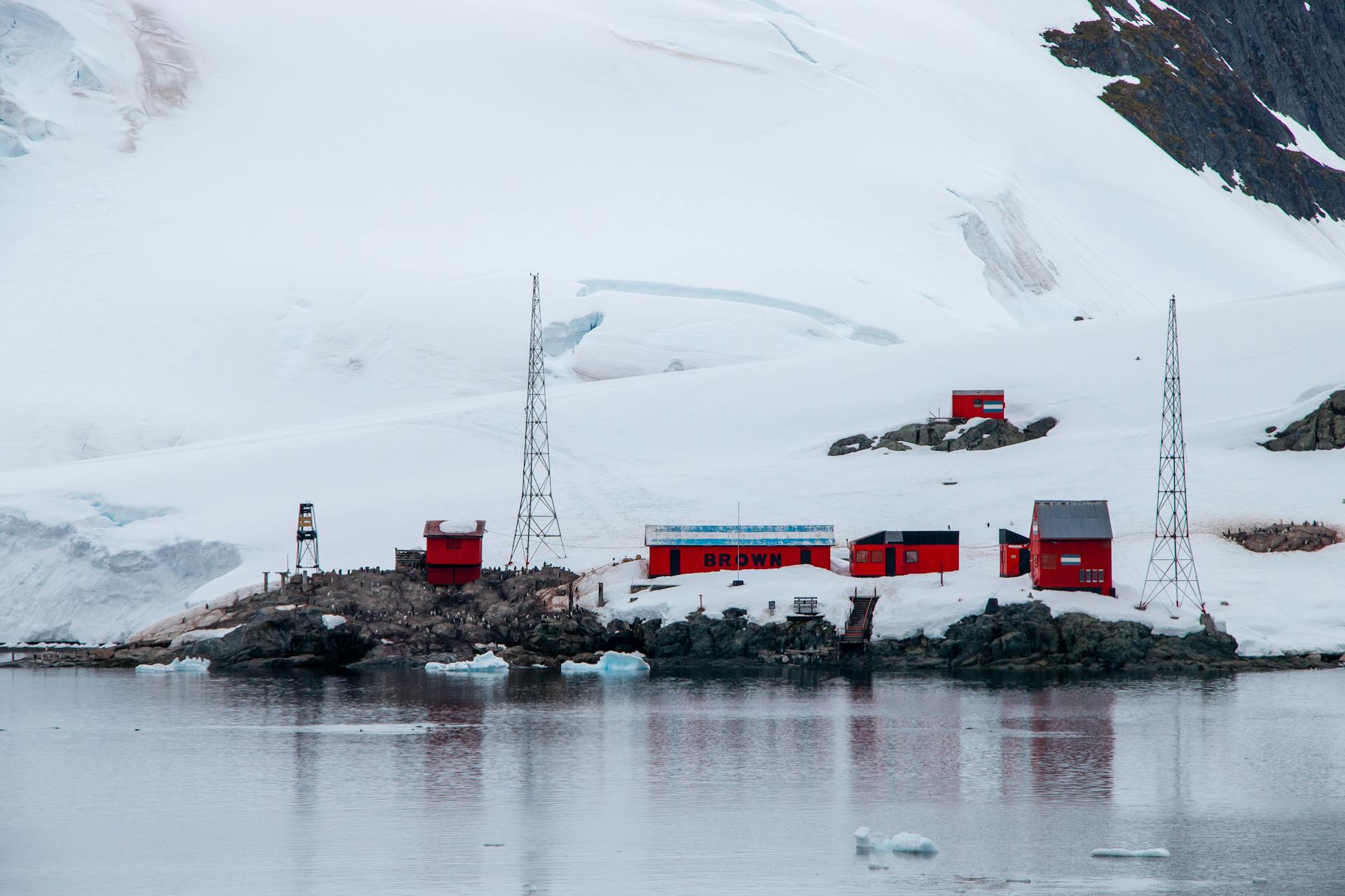 Red research station nestled in Antarctica's icy landscape by the sea, showcasing remote exploration.