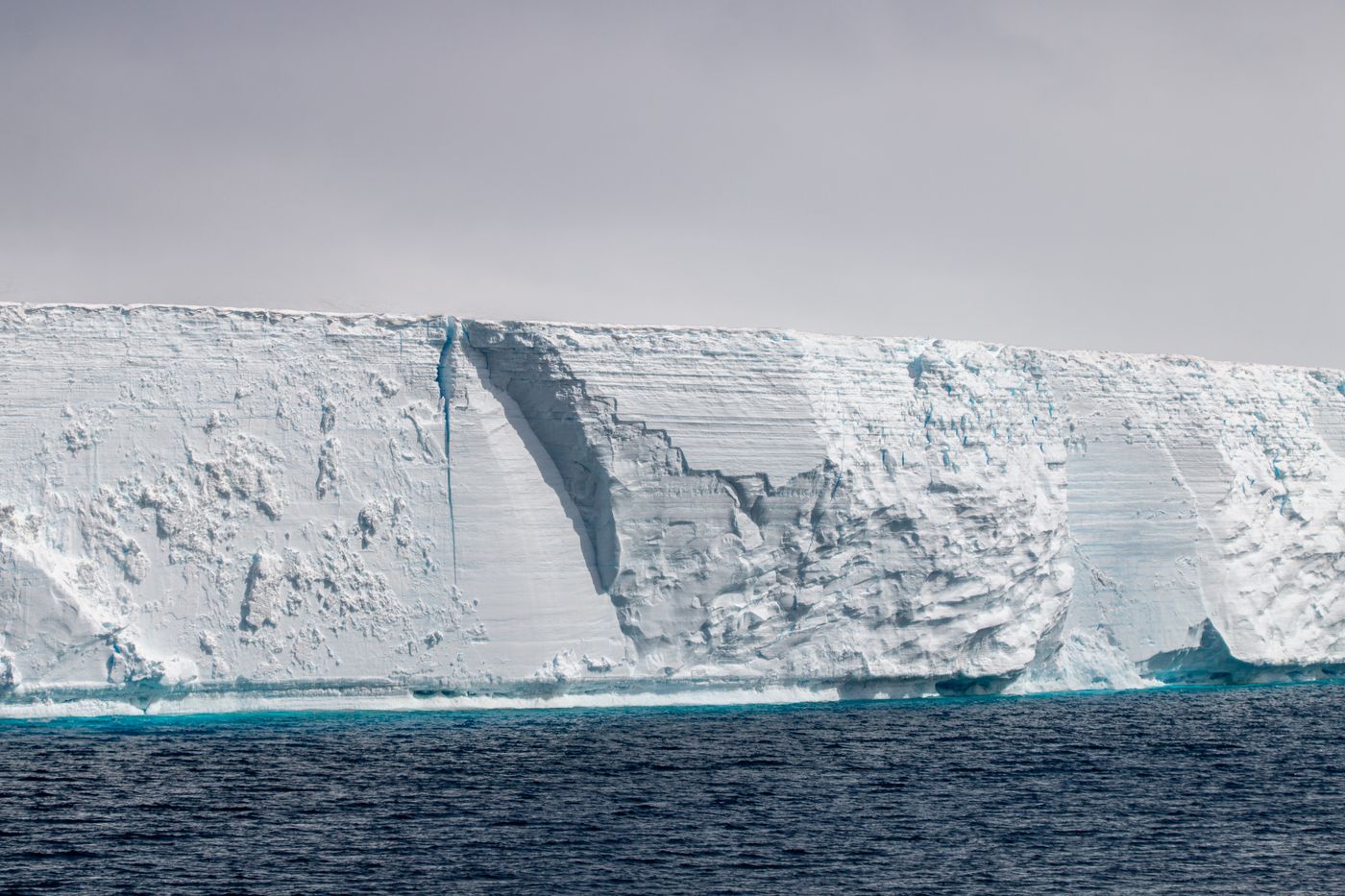 A large iceberg with steep ice cliffs floating in calm water in Antarctica
