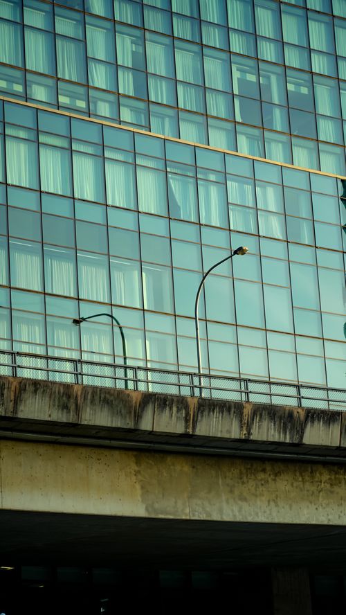 Free Glass facade of a modern building with highway and streetlights in foreground. Stock Photo