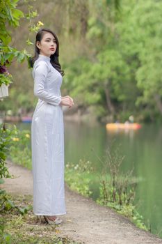 Woman in white dress standing by a serene lake surrounded by lush greenery.