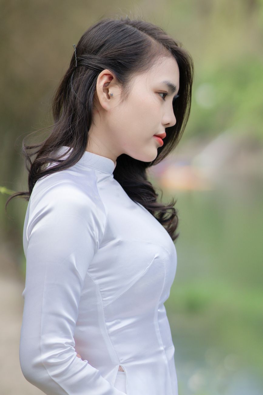 Elegant woman in white dress by serene waterside, showcasing cultural attire.