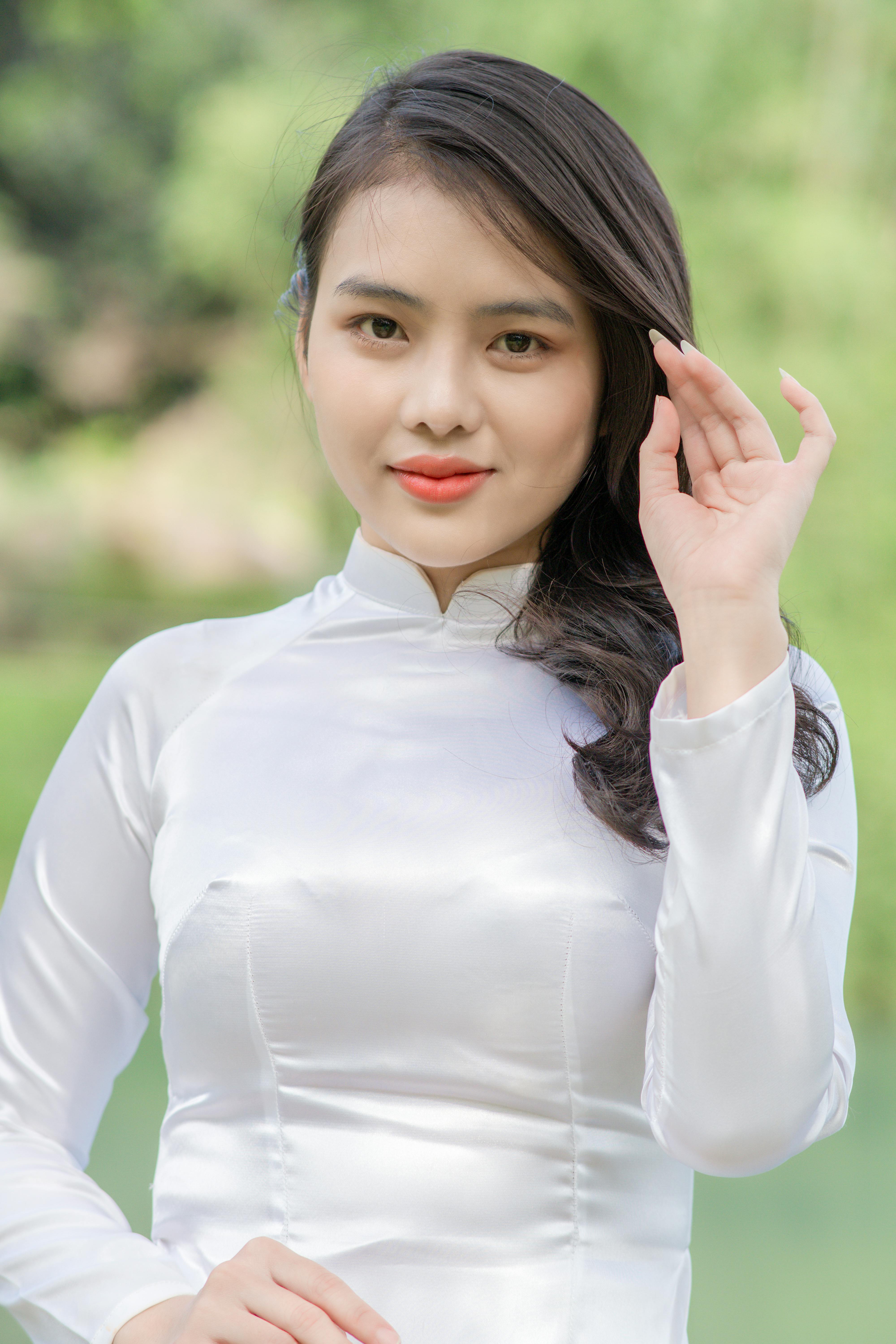 A woman in a white Ao Dai poses outdoors against a green nature background.