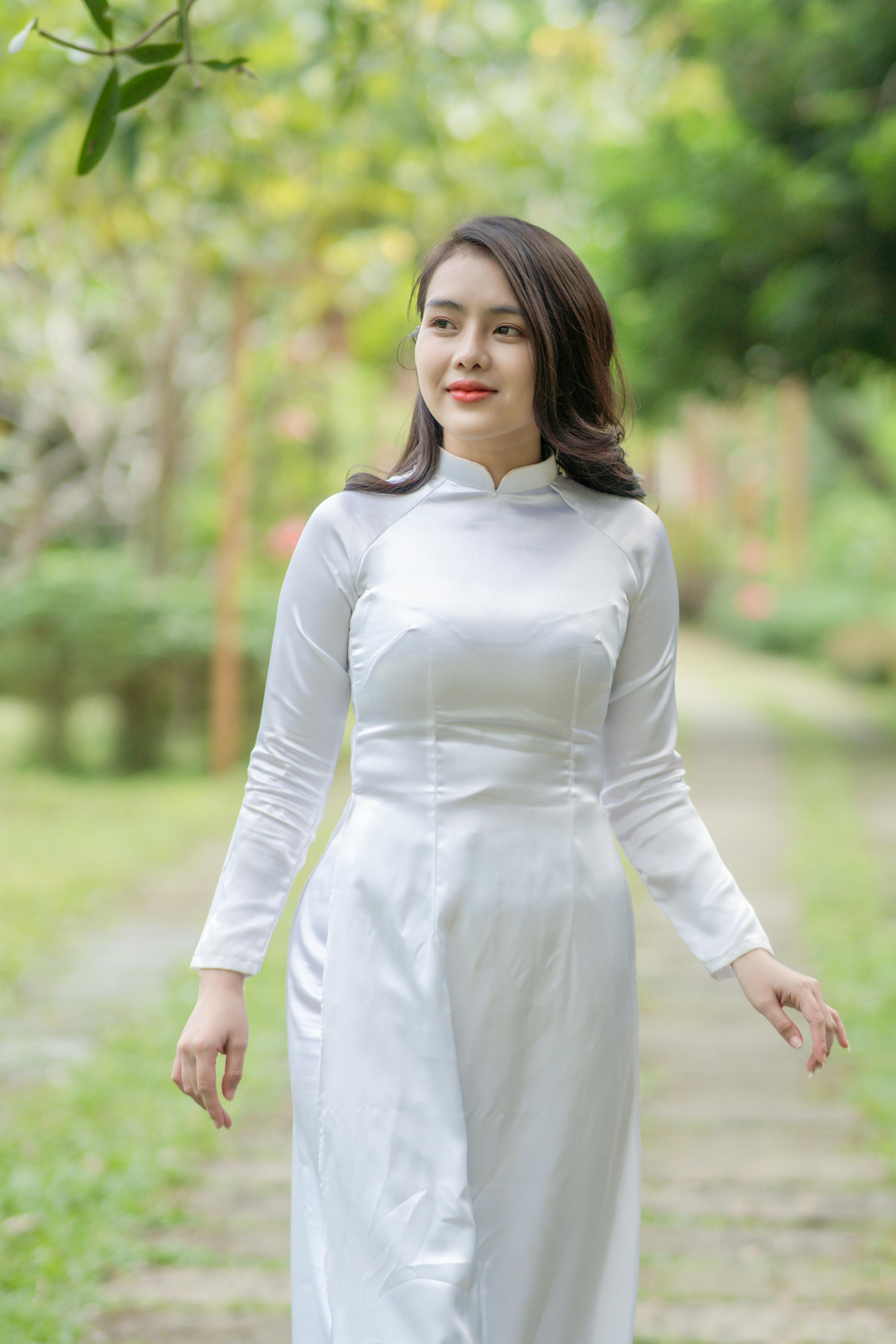 Elegant woman in white Ao Dai walking through a lush garden path, exuding grace and tradition.