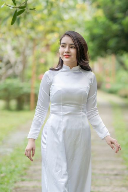 Elegant woman in white Ao Dai walking through a lush garden path, exuding grace and tradition.