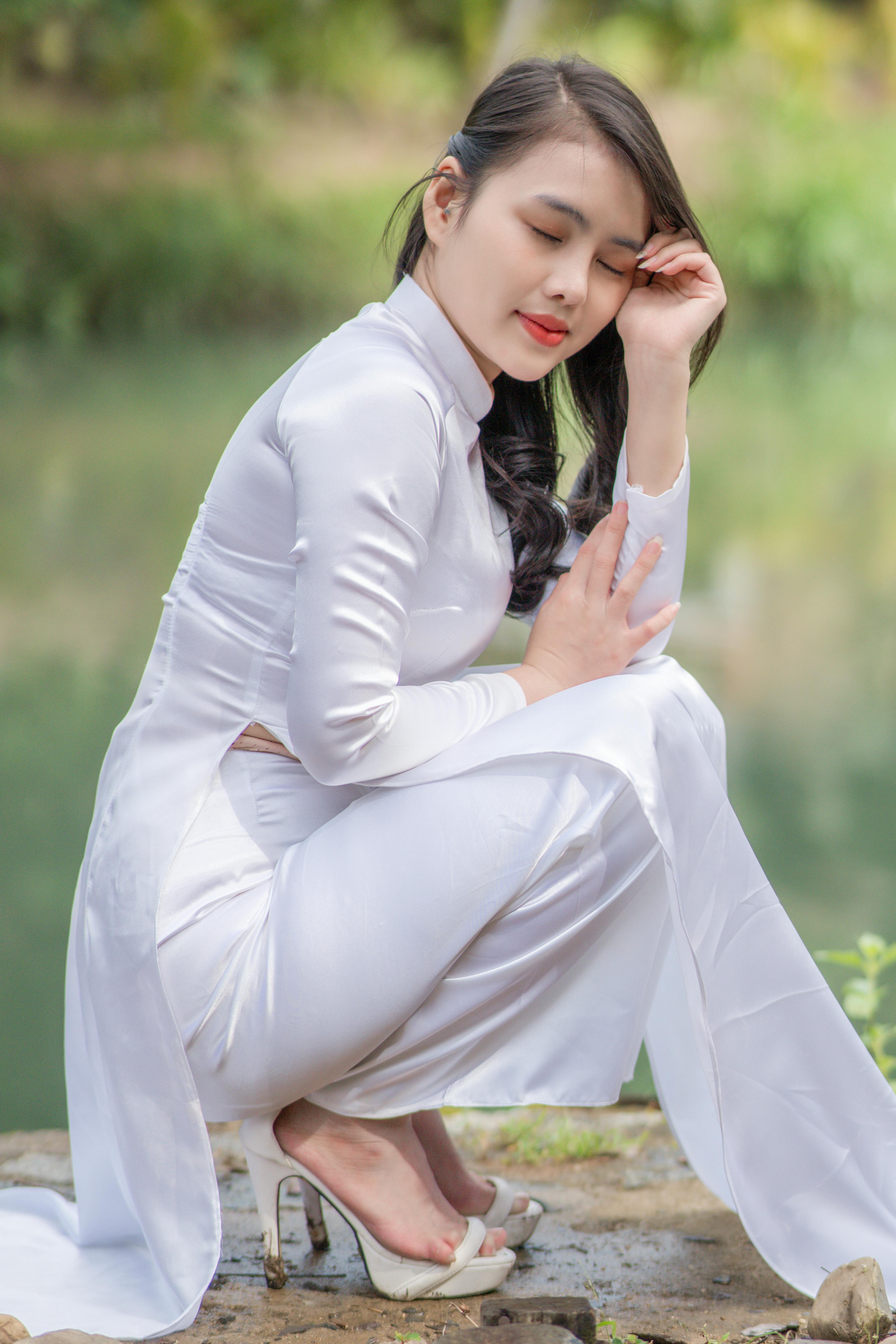 Young woman in traditional white Ao Dai dress poses by a tranquil pond.