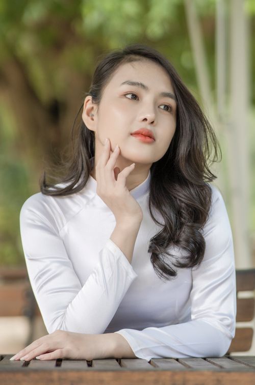Free Portrait of a woman in white attire, seated outdoors, exuding elegance and poise. Stock Photo