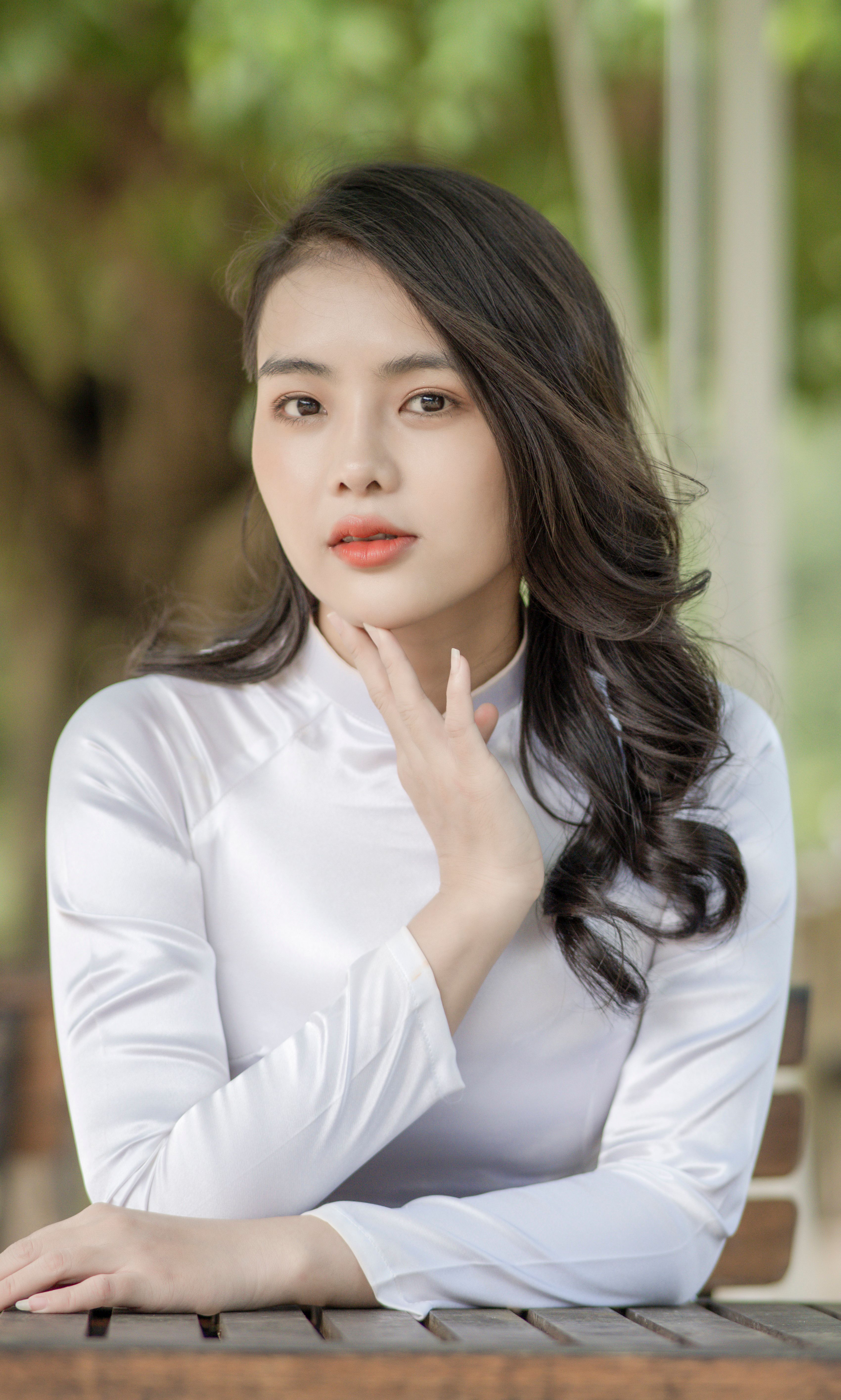 A serene portrait of a woman in a white top, outdoors with a natural background.