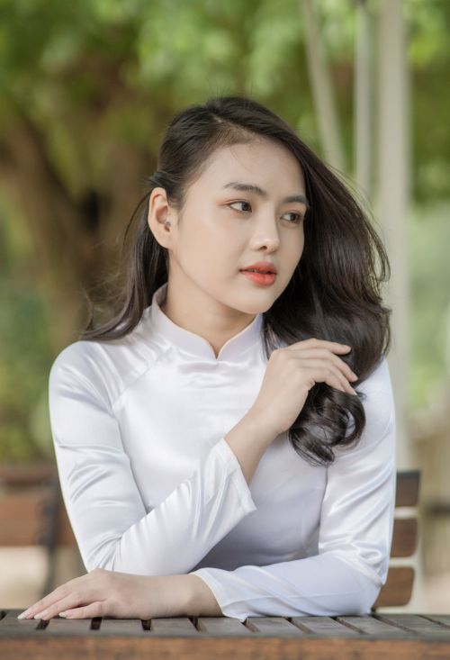 Free Elegant portrait of a woman in a white dress with a serene expression, seated outdoors. Stock Photo