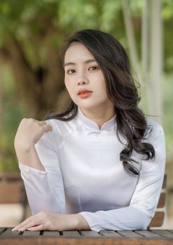 Portrait of a woman in a white traditional dress with lush green background.