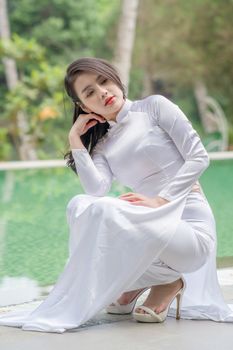 Woman in traditional white attire posing elegantly by the poolside outdoors.
