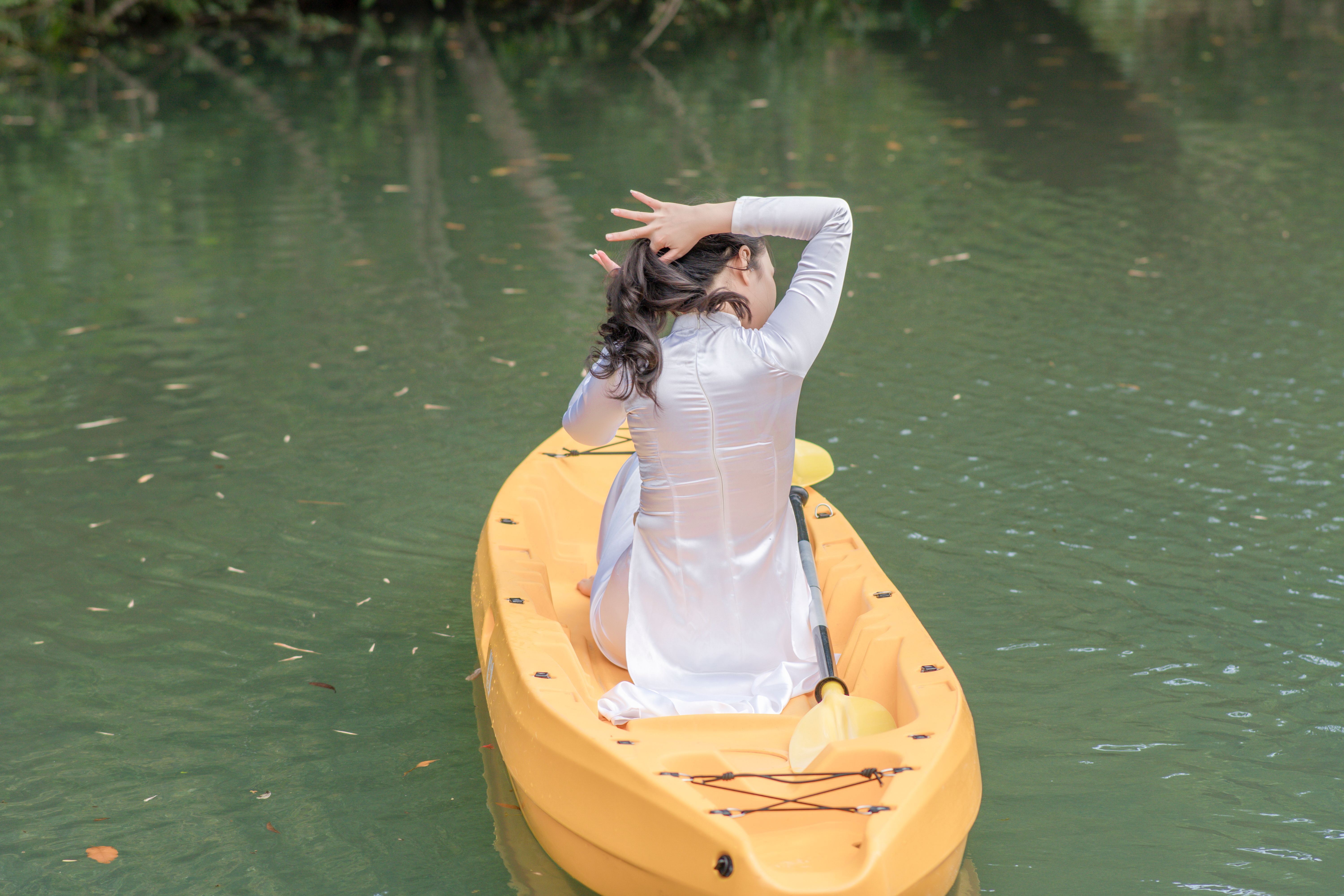A peaceful scene of a woman in a white dress kayaking on a calm lake.