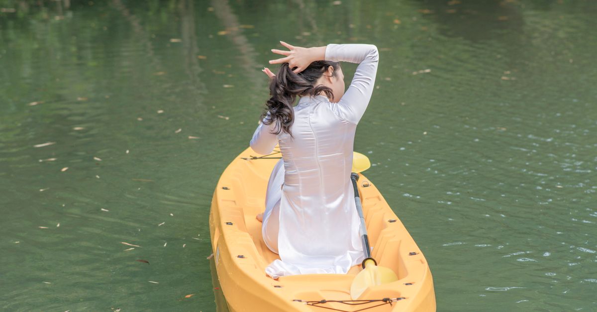 A peaceful scene of a woman in a white dress kayaking on a calm lake.