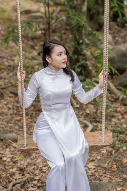 Portrait of a young woman in a white Ao Dai sitting on a swing outdoors.