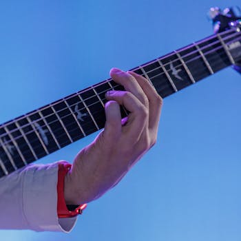 Close-up of a hand playing an electric guitar on a blue background.