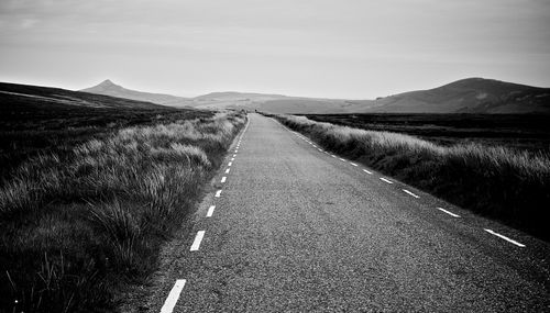Free Black and white image of a long, empty highway stretching through a vast, open landscape with distant hills. Stock Photo