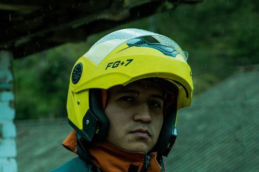 A serious man wearing a yellow safety helmet stands outdoors in rain, conveying protection and focus.