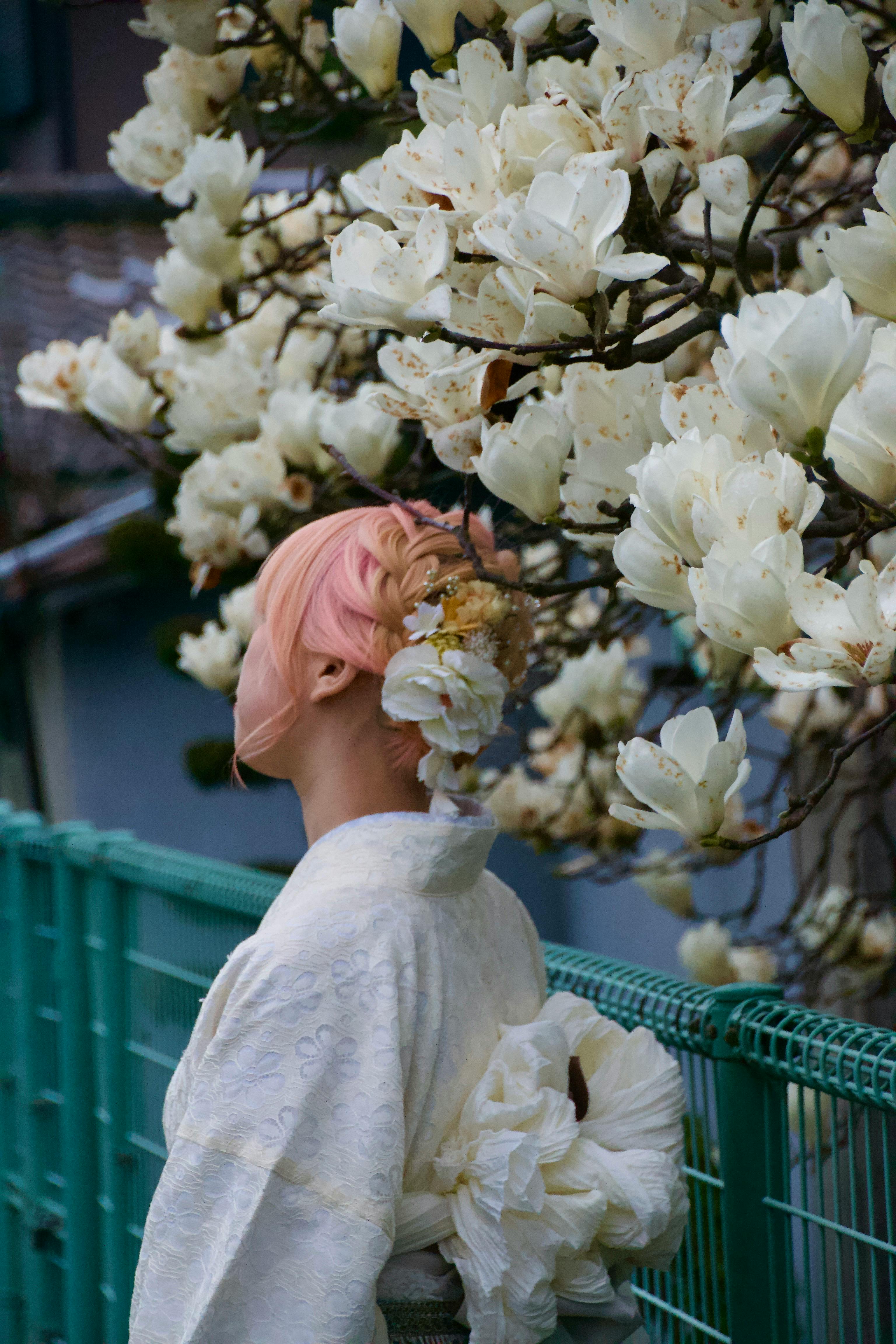 A woman in a kimono stands near magnolia blossoms, exuding traditional elegance.