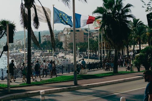 Free Explore the bustling Nice seaside promenade with flags waving and crowds enjoying a sunny summer day. Stock Photo