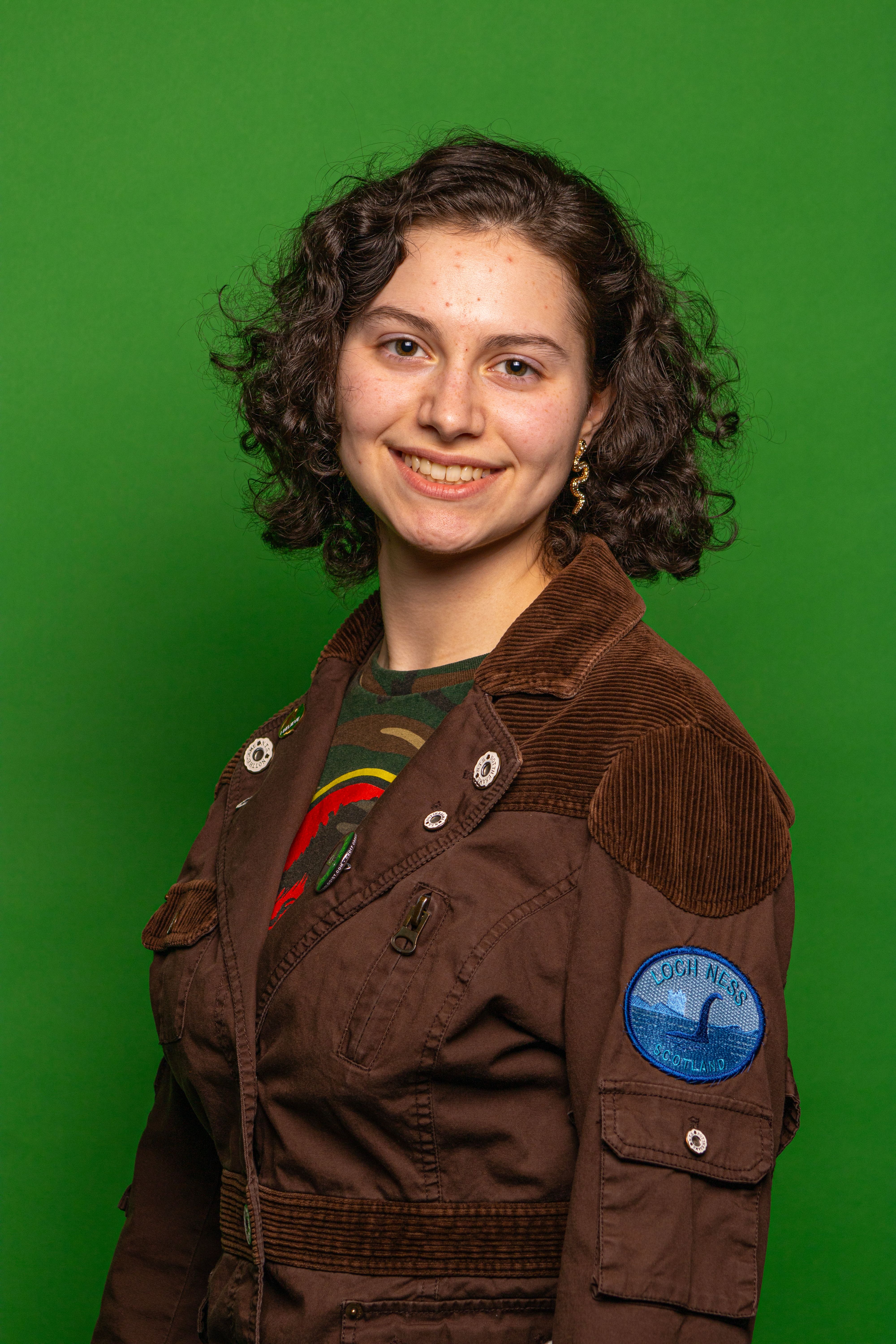 Portrait of a smiling woman in a brown jacket against a vibrant green background.