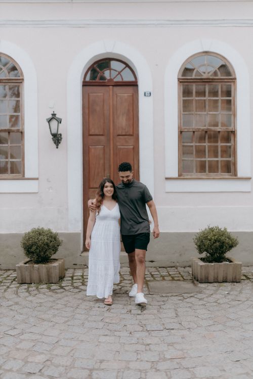Free Happy couple walking arm-in-arm outside a vintage building with wooden doors and arched windows. Stock Photo