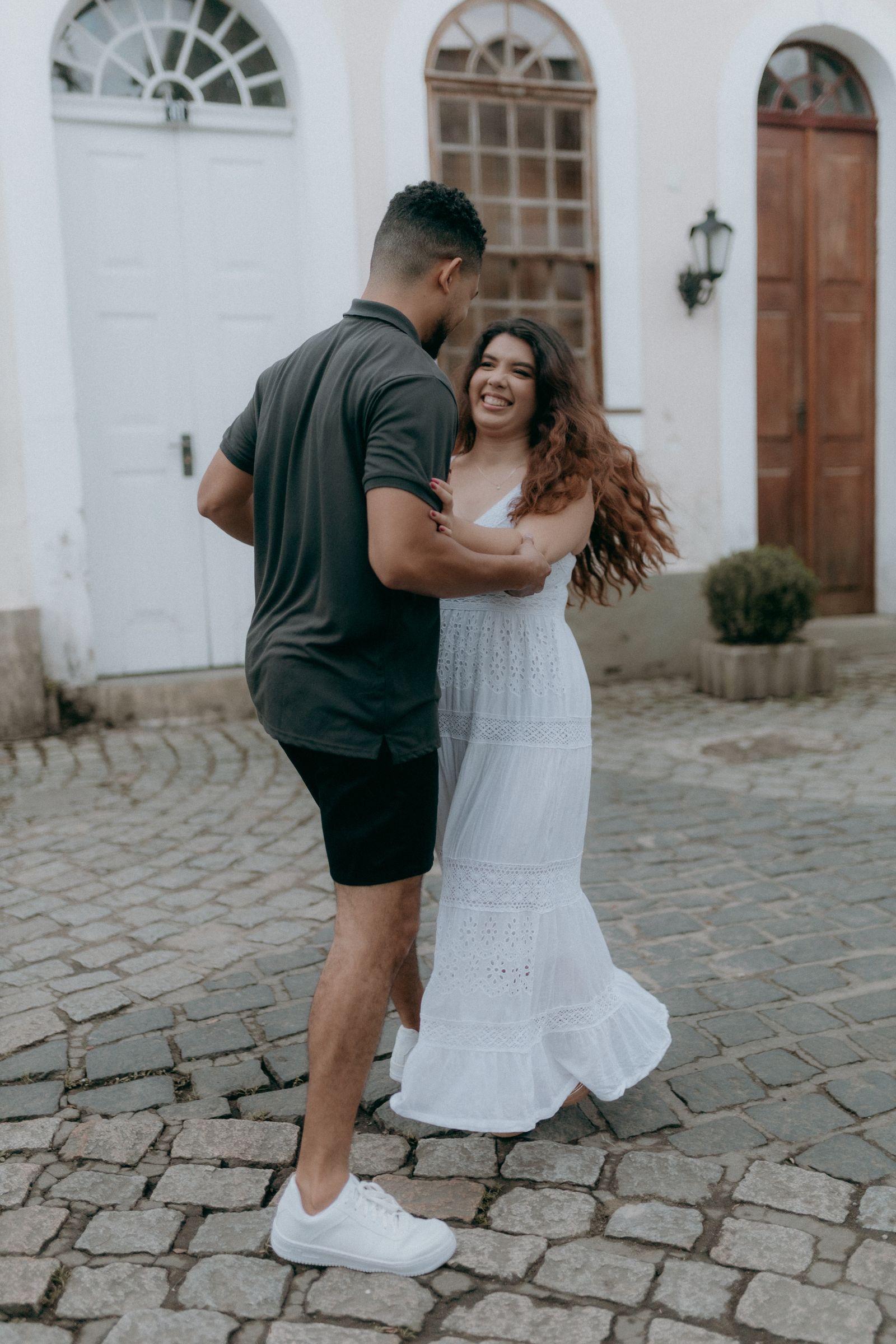 Your first step — couple dancing on a cobblestone street, laughing. Stock photo.