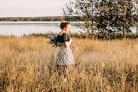 阳光明媚的田野上，一名年轻女子站在湖边，手里拿着薰衣草花，微笑着