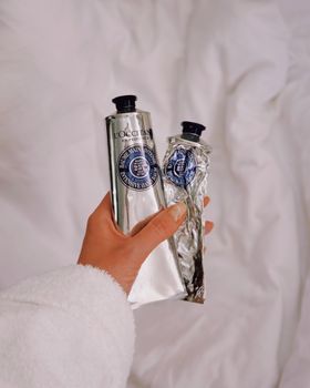 Close-up of hand holding L'Occitane creams, symbolizing luxury skincare routine.