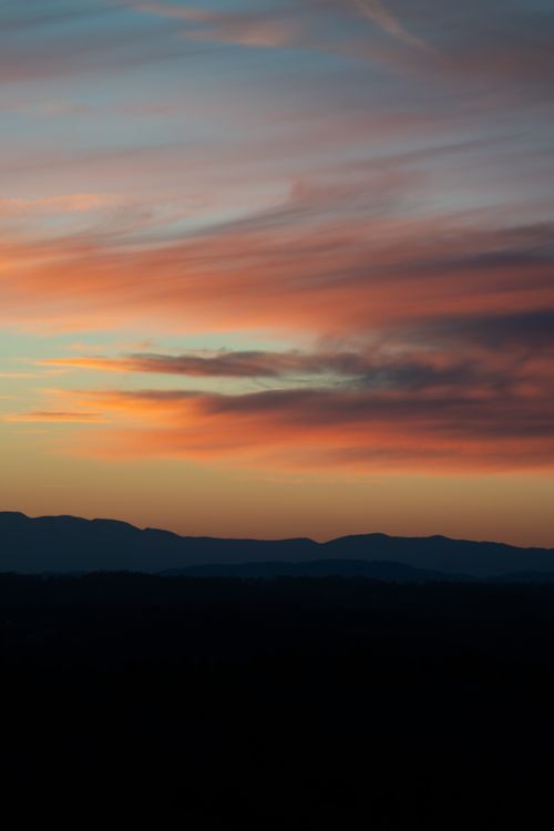 Free A breathtaking sunset with vibrant clouds over a serene mountain landscape, perfect for calming desktop backgrounds. Stock Photo