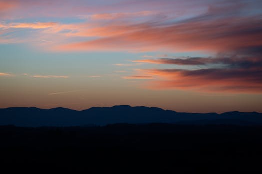 Serene sunset view with vibrant clouds and silhouetted hills, perfect for wallpaper use.