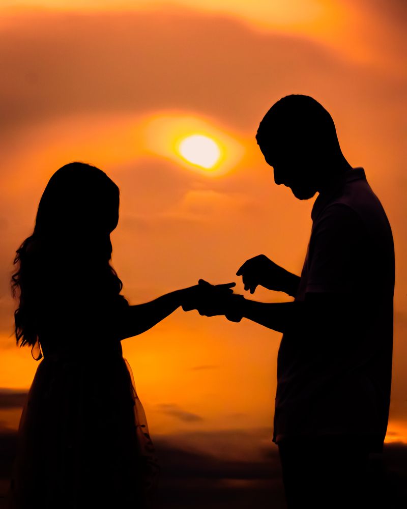 A couple in silhouette holding hands against a sunset sky