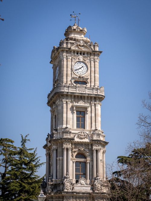 Free A beautifully detailed historic clock tower set against a clear blue sky with surrounding trees. Stock Photo