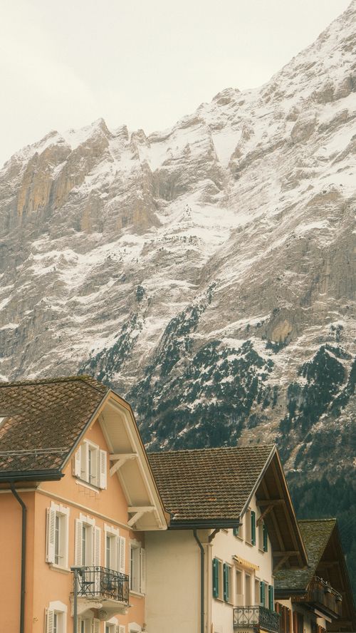 Free Alpine village with snow-covered mountains, showcasing traditional European architecture. Stock Photo