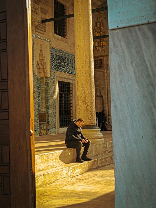 Free A serene scene of a man sitting in a sunlit historic architectural setting, showcasing intricate tilework. Stock Photo