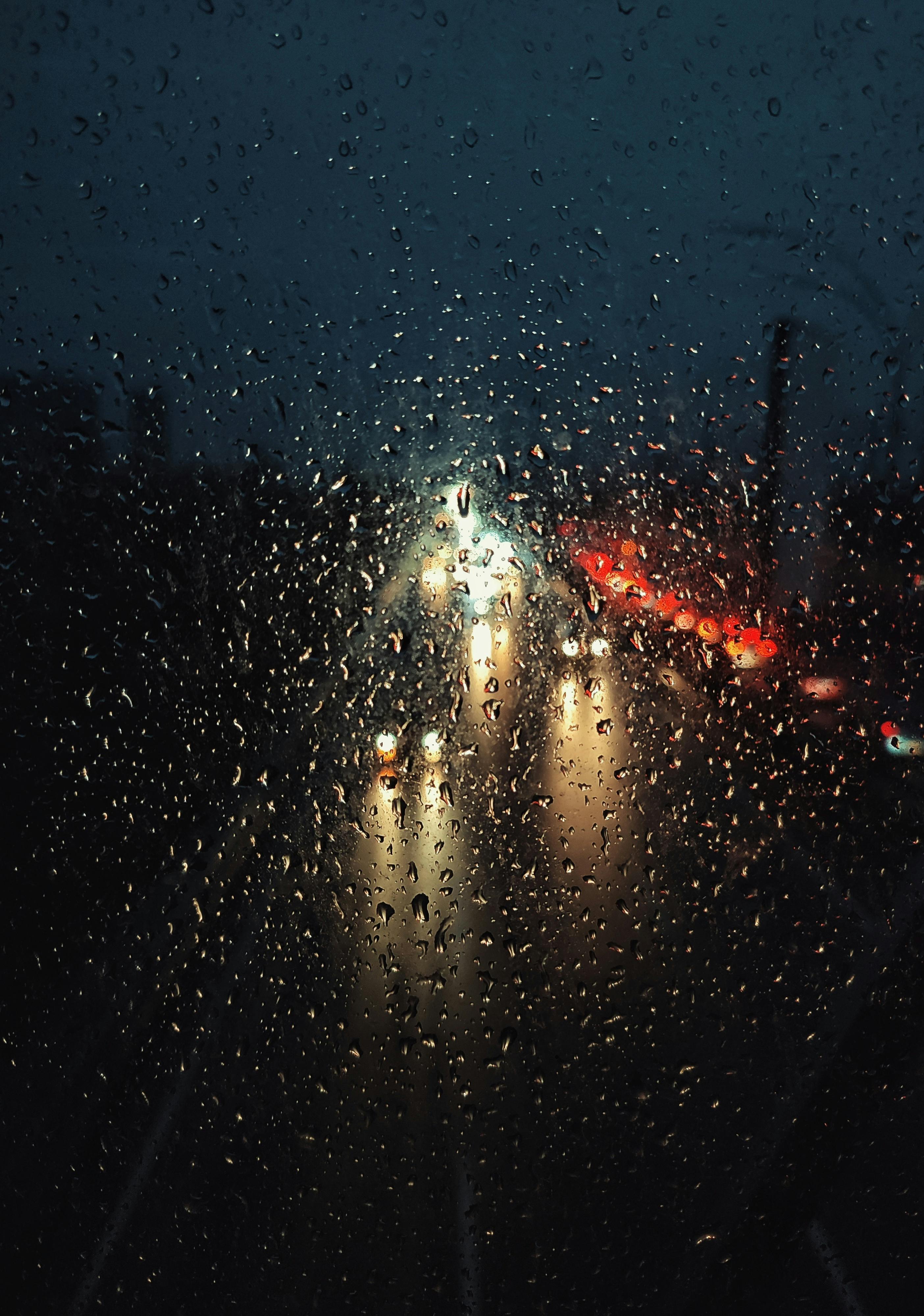 Blurry traffic lights seen through raindrop-covered window on a rainy night.