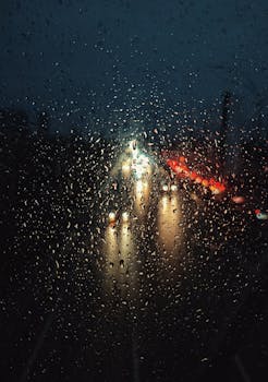 Blurry traffic lights seen through raindrop-covered window on a rainy night.
