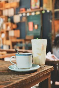 Warm café setting with a cup of coffee and a refreshing iced drink on a wooden table.