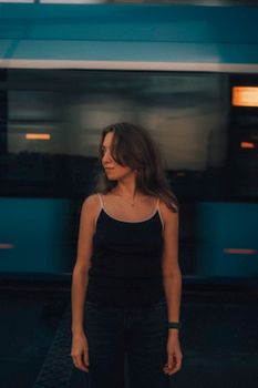 Woman in dark attire stands still as train rushes by at dusk, creating motion blur effect.