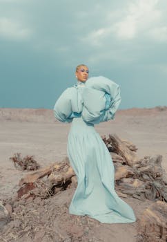 Elegant model in stylish blue gown poses against a dramatic desert backdrop.