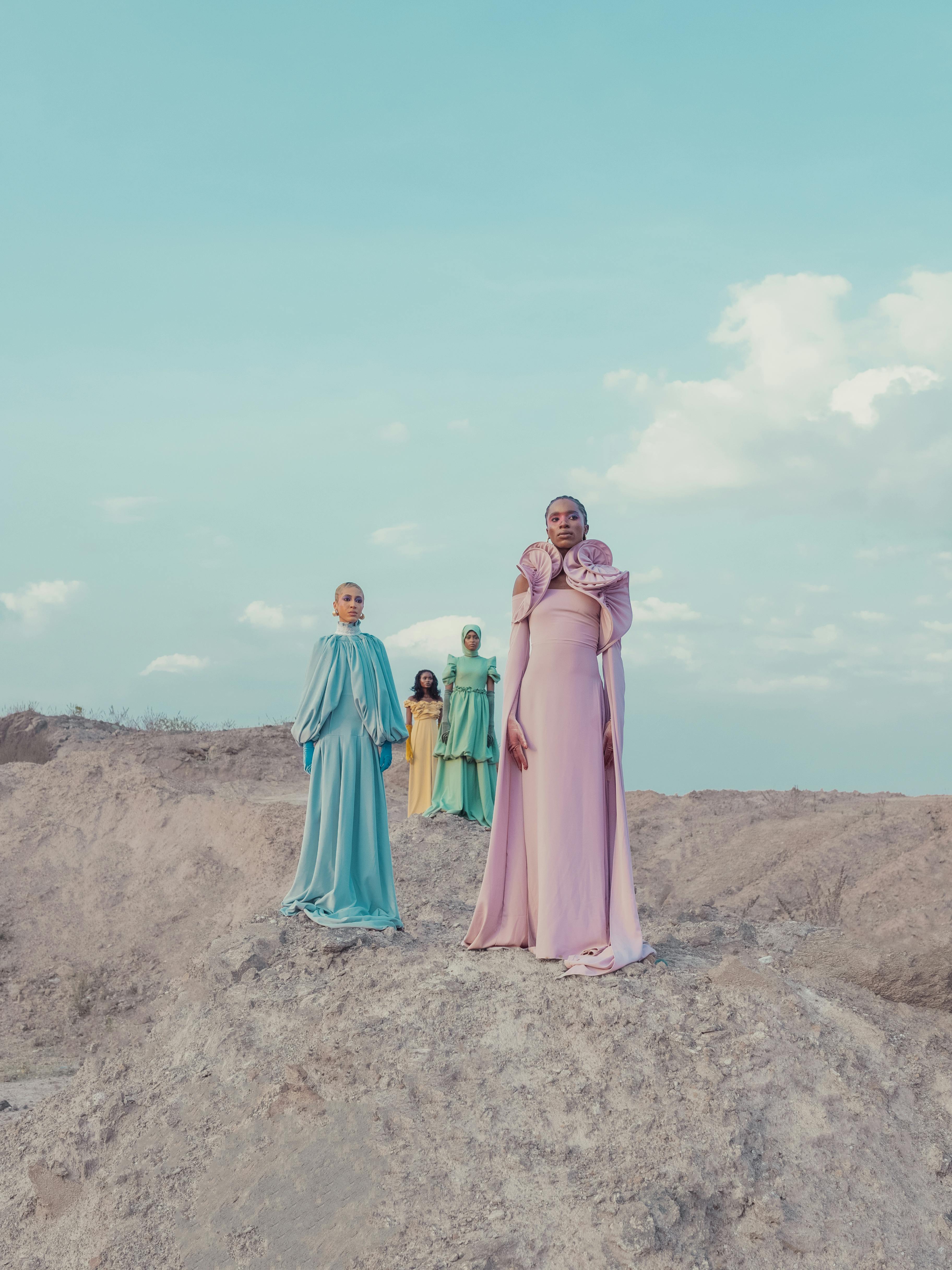 Zadarmo Štyri ženy vo farebných splývavých šatách pózujúce v neskutočnej, pustej krajine pod modrou oblohou. Fotka z fotobanky