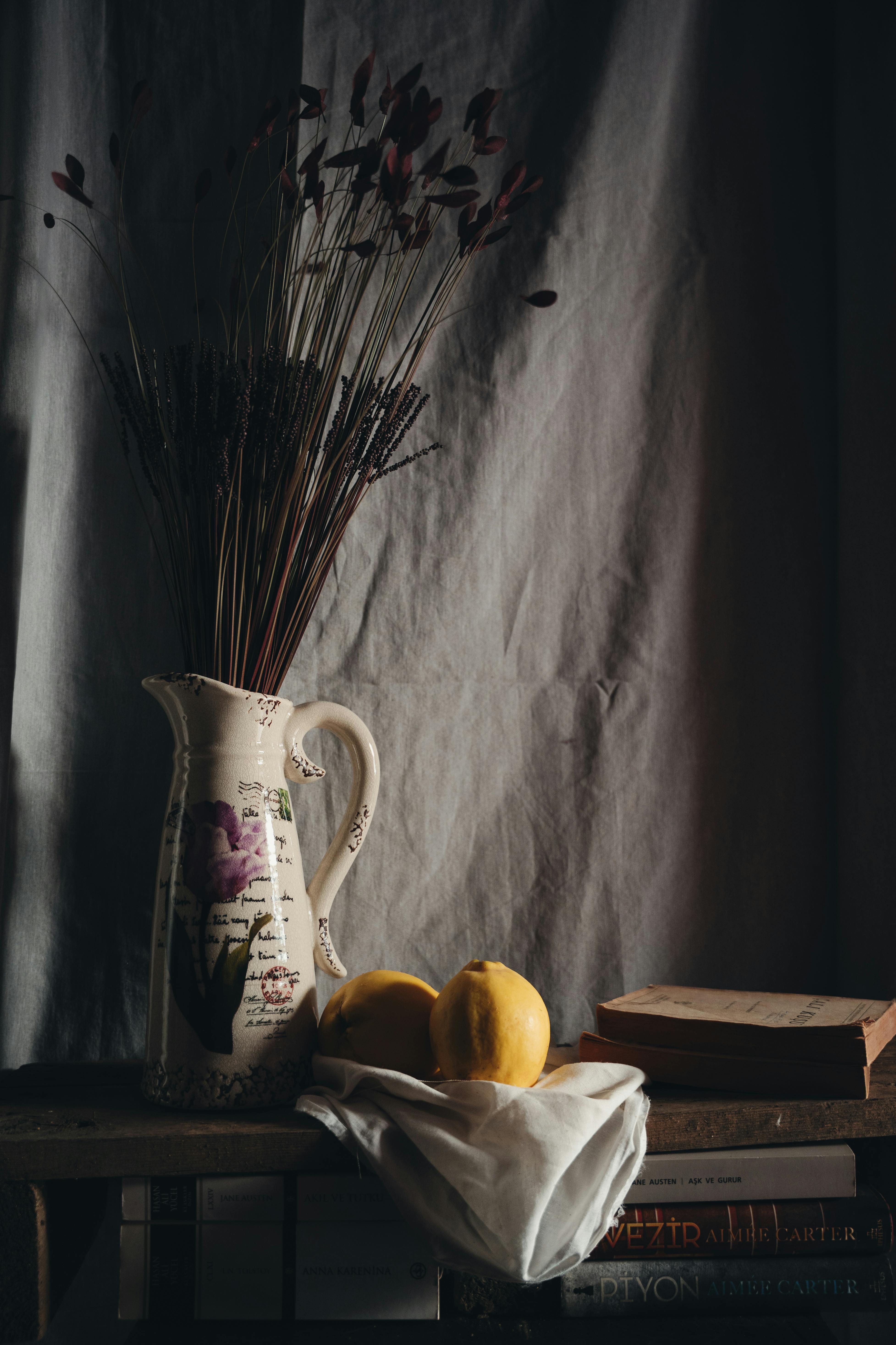 A classic still life composition with a floral vase, old books, and bright lemons on a wooden shelf.