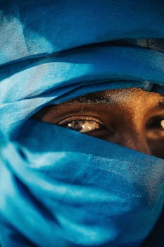 Close-up of a person's eye peeking through a vibrant blue fabric veil, evoking mystery.