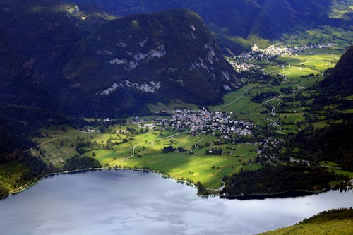 Aerial view settlements on grassy peaceful valley surrounded with green hills and calm river on sunny day