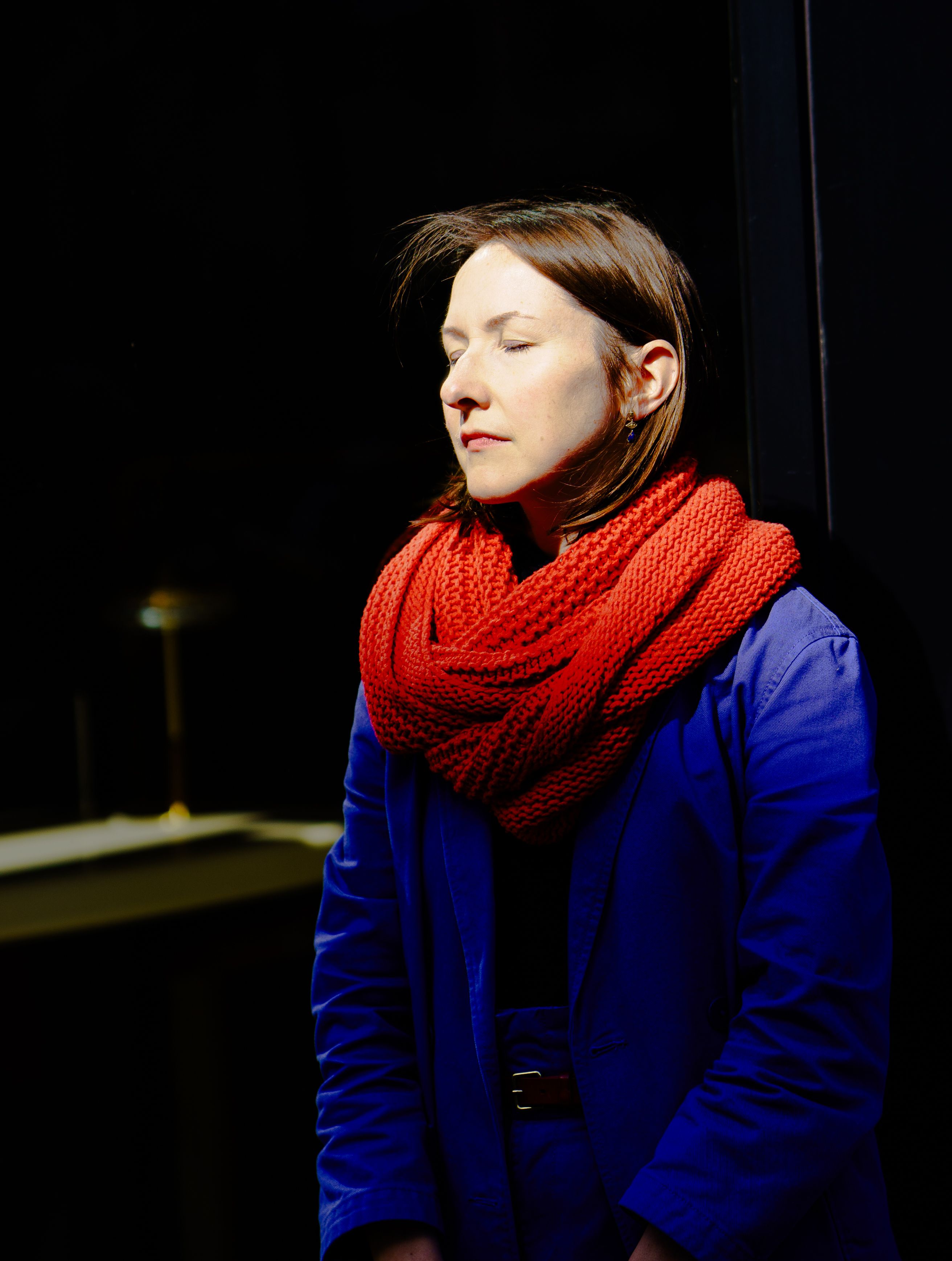 Portrait of a woman with eyes closed, warmly illuminated by sunlight, wearing a bright red scarf in Cambridge.