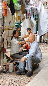 A barber cuts an older man's hair on a bustling outdoor street corner.