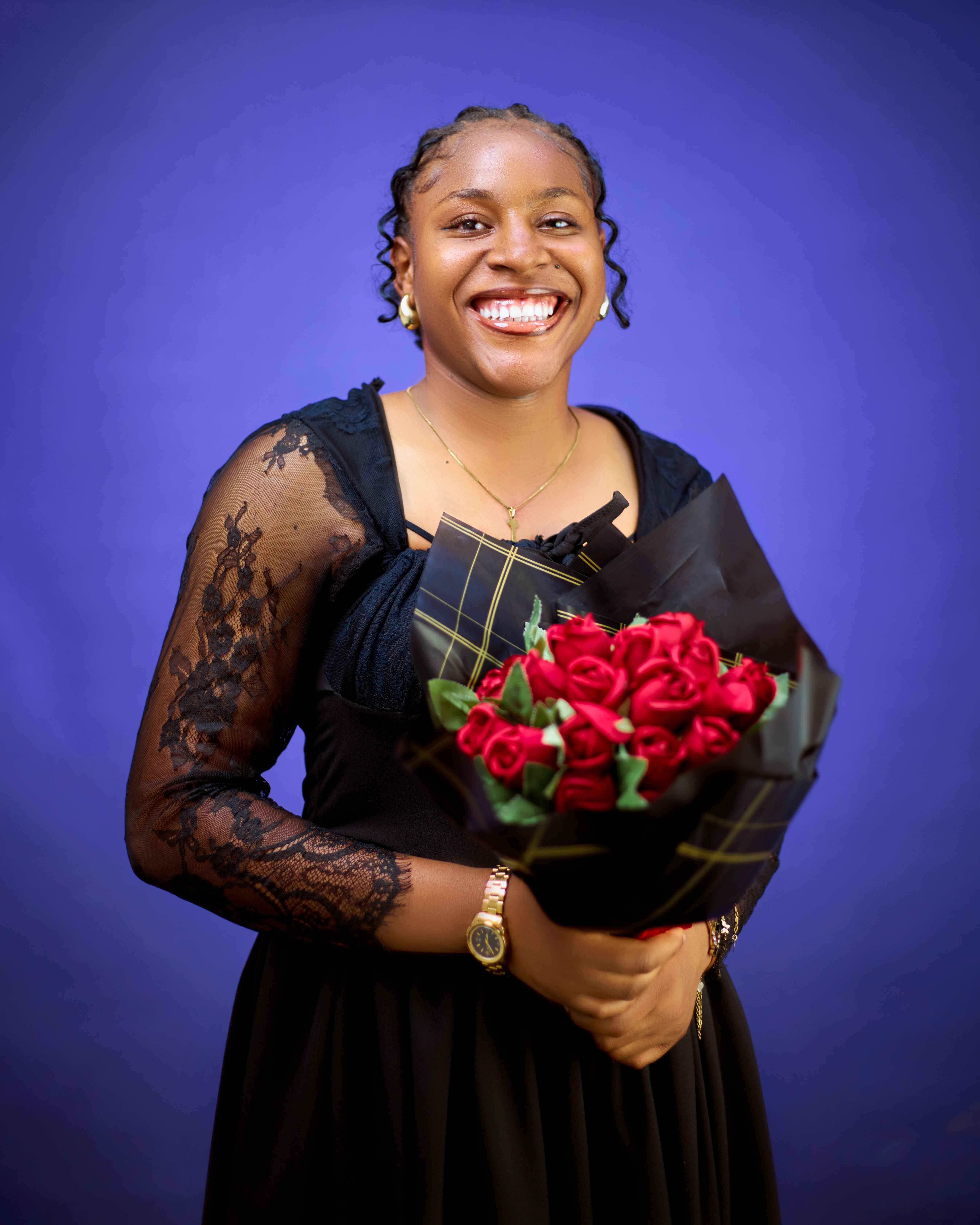 Joyful woman in black lace dress holding a bouquet of red roses against a vibrant blue backdrop.