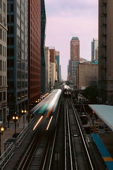 Captivating cityscape featuring blurred trains in motion between tall buildings at dusk.