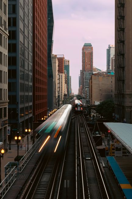 Captivating cityscape featuring blurred trains in motion between tall buildings at dusk.